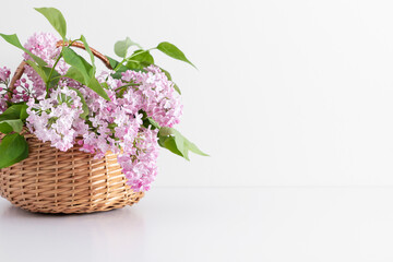 Bouquet of lilacs in basket on white table. Front view.