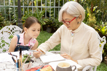 Asian grandmother is drawing outside with two granddaughter. Casual, outdoors, nature