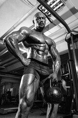 Obraz na płótnie Canvas Bodybuilder athlete trains in the gym. Sporty muscular guy with athletic kettlebell. Sport and fitness motivation. Individual sports recreation with bodybuilding.