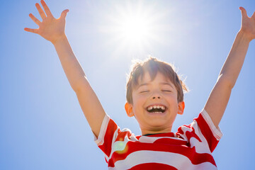 Happy boy raising hands over blue sky with sun. Feel freedom , enjoying life and nature. Summer holidays concept © Elena