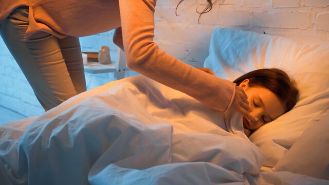 Woman Covering Blanket On Sleeping Child In Bedroom