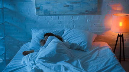 Floor lamp near woman sleeping on bed during night