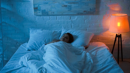 Woman sleeping on bed near floor lamp in bedroom