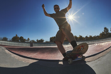 Young man doing a trick on skateboard in a skatepark bowl with sun backlight