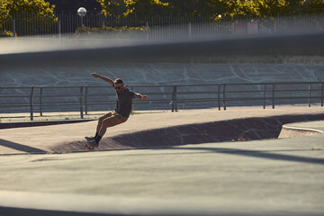 Young man skater doing a turn in a skatepark bowl at sunrise