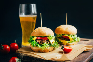close-up of a hamburger with meat on a grill tomato and greens on the background of a glass with beer on a black background