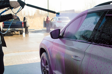 close-up -  a man at a car wash washing his own white car with a high pressure water spray gun