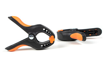 Plastic spring clamp isolated on white background. Clamping equipment. Working hand tool. Black and orange spring clamp. Closeup..