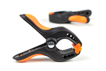 Fototapeta premium Plastic spring clamp isolated on white background. Clamping equipment. Working hand tool. Black and orange spring clamp. Closeup..