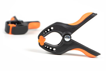 Obraz premium Plastic spring clamp isolated on white background. Clamping equipment. Working hand tool. Black and orange spring clamp. Closeup..