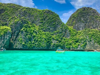 Grüne Vulkaninsel in Thailand mit türkis klarem Wasser umgeben und Booten