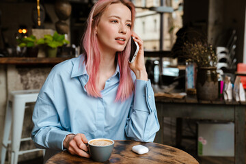 Young white woman talking on mobile phone while drinking coffee
