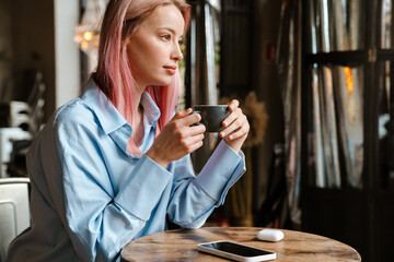 Young white woman with pink hair drinking coffee while sitting in cafe