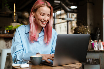 Young smiling woman with pink hair working with laptop in cafe