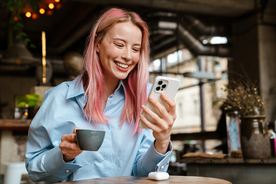 Young smiling woman using mobile phone while drinking coffee in cafe