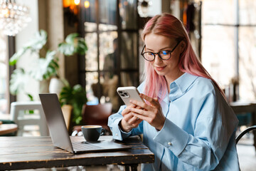Young woman using laptop and cellphone while sitting in cafe