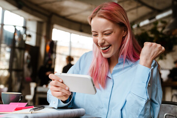 Young woman with pink hair using cellphone while studying in cafe