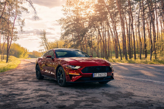 American muscle car Ford Mustang in a red color on the forest road. Kherson, Ukraine - May 2021.