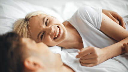 Obraz na płótnie Canvas happy woman laughing while lying on bed with boyfriend on blurred foreground