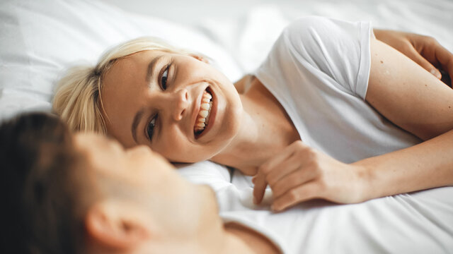 cheerful woman laughing while lying on bed with boyfriend on blurred foreground