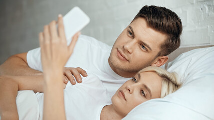 young man and woman taking selfie on smartphone in bedroom