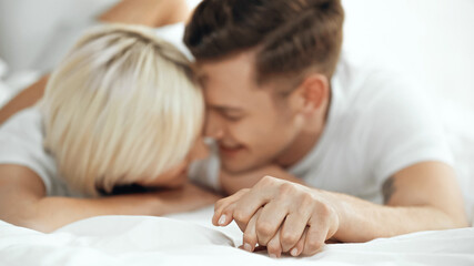 Fototapeta na wymiar blurred young couple holding hands and smiling in bed