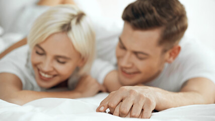 Obraz na płótnie Canvas blurred happy woman and man holding hands and smiling in bed