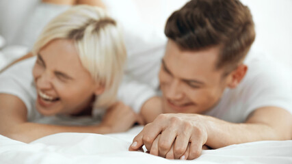 blurred young woman and man holding hands and laughing in bed