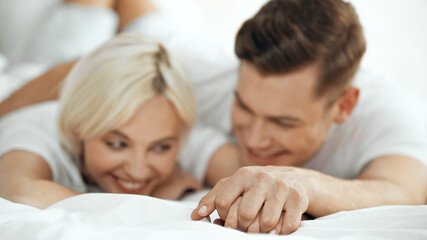 blurred young man and woman holding hands and smiling in bed