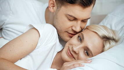 Obraz na płótnie Canvas young man kissing cheek of happy blonde girlfriend