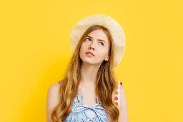 Dreaming young woman, in summer clothes and in a straw hat, on a yellow background, thinking concept