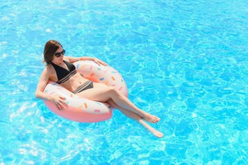 Beautiful woman and inflatable swim ring in shape of a donut in the pool
