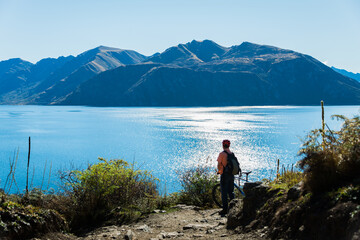 Cyclist standing with his bike enjoying the views of the Lake Wanaka on Glendhu Bay track, South Island.