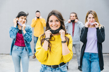 Portrait of a group of young millennial friends lower the mask and smile -Tools need to wearing avoid the infection from Coronavirus, Covid-19 - People having fun together - Concept of freedom