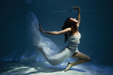 lighting on graceful woman in white elegant dress swimming in pool with blue water
