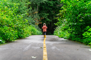 a child in yellow boots runs along the path in the park