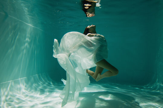 peaceful young woman in white elegant dress swimming in pool