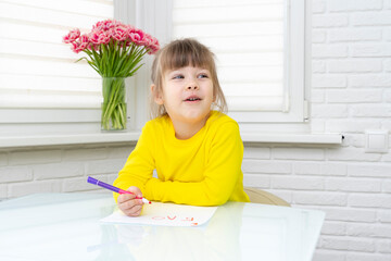 little girl sits at a table in a white room and draws