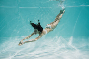 graceful young woman in white swimsuit diving in pool