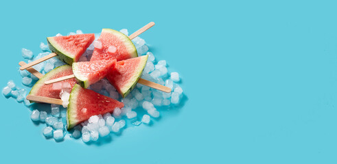 Watermelon slices popsicles and ice on blue background. Panorama view
