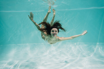 cheerful young woman in white swimwear swimming in pool