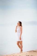 Beautiful woman in a white dress walking on the beach.Relaxed woman breathing fresh air,emotional sensual woman near the sea, enjoying summer.Travel and vacation. Freedom and inspiration concept