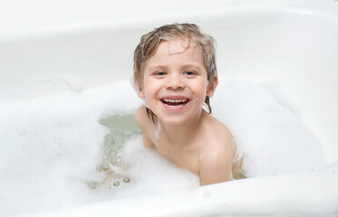 the child sits in the bath in the water with foam and laughs, makes a funny expression on his face....