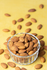 Pile of peeled raw almonds in a bowl and on a yellow table