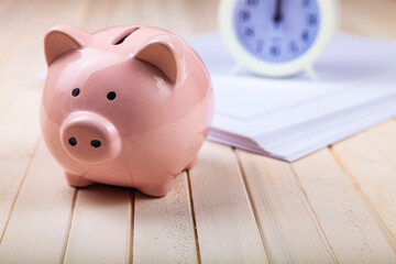 Pig piggy bank, paper and clock on a white wooden background.