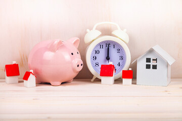 Pink piggy bank and small houses on the background of the clock.