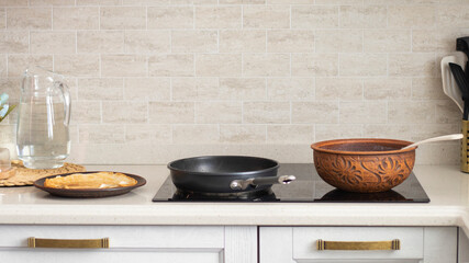 The process of making thin pancakes in a cozy home kitchen. Pancakes in a frying pan and in earthenware. Thin pancakes close-up. Light kitchen interior. 