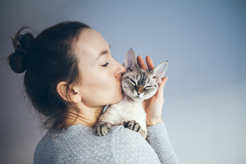 Woman is kissing and cuddling her sweet and cute looking Devon Rex cat. Kitten feels happy to be with its owner.  Kitty sits in humans arms purrs.