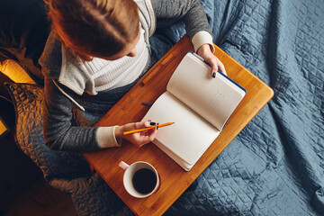 Obraz premium Student learning at home. Young woman making notes, reading and learning from notepad. Girl writing journal sitting in bed