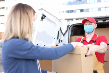Male courier wearing protective medical mask giving cardboard box to woman